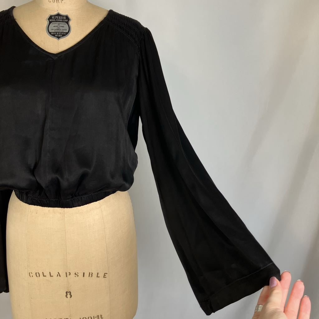 A black long-sleeve blouse displayed on a beige dress form mannequin, with a hand pointing to the sleeve cuff against a light gray fabric backdrop.
