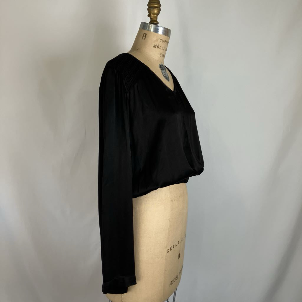 A black long-sleeve blouse with a V-neck and gathered shoulders, displayed on a beige dress form mannequin against a light gray fabric backdrop.