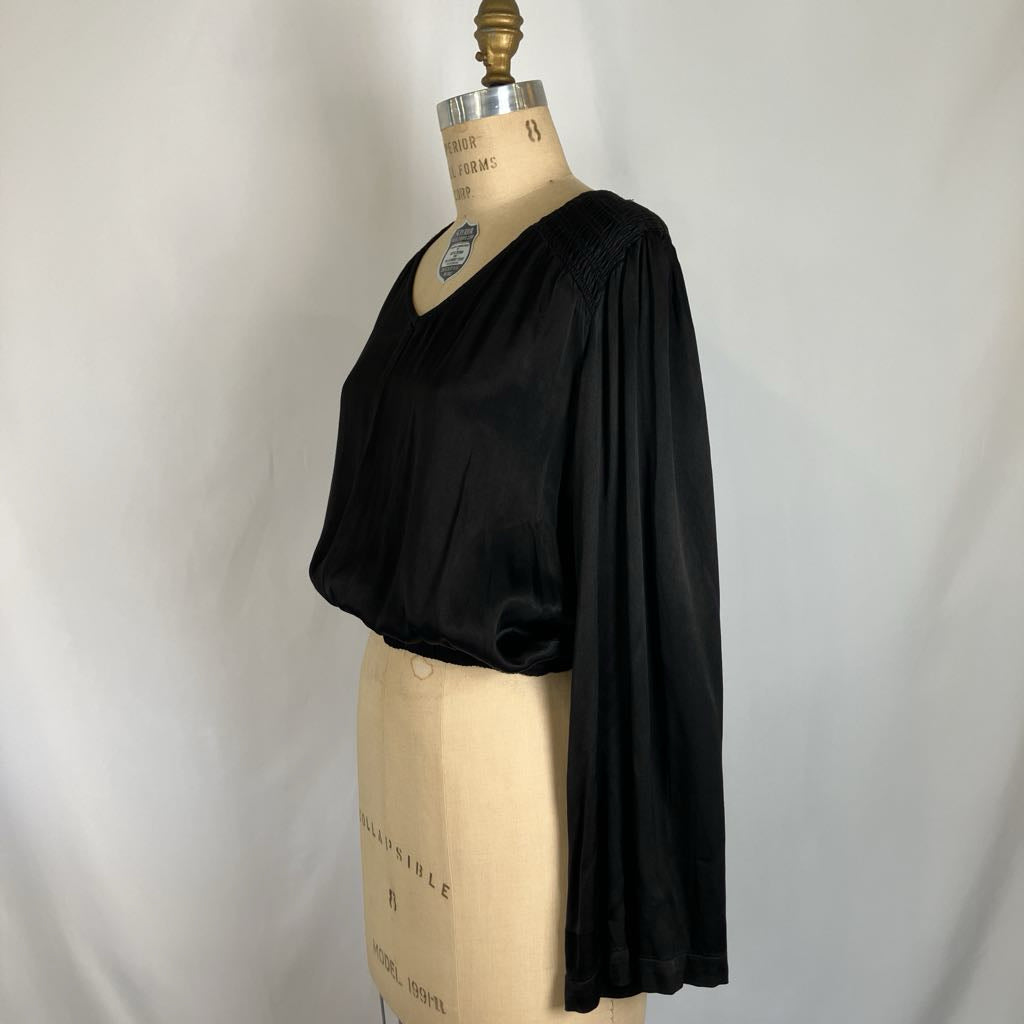 A black long-sleeve blouse with a V-neck and gathered, draped sleeves, displayed on a beige dress form mannequin against a light gray fabric backdrop.