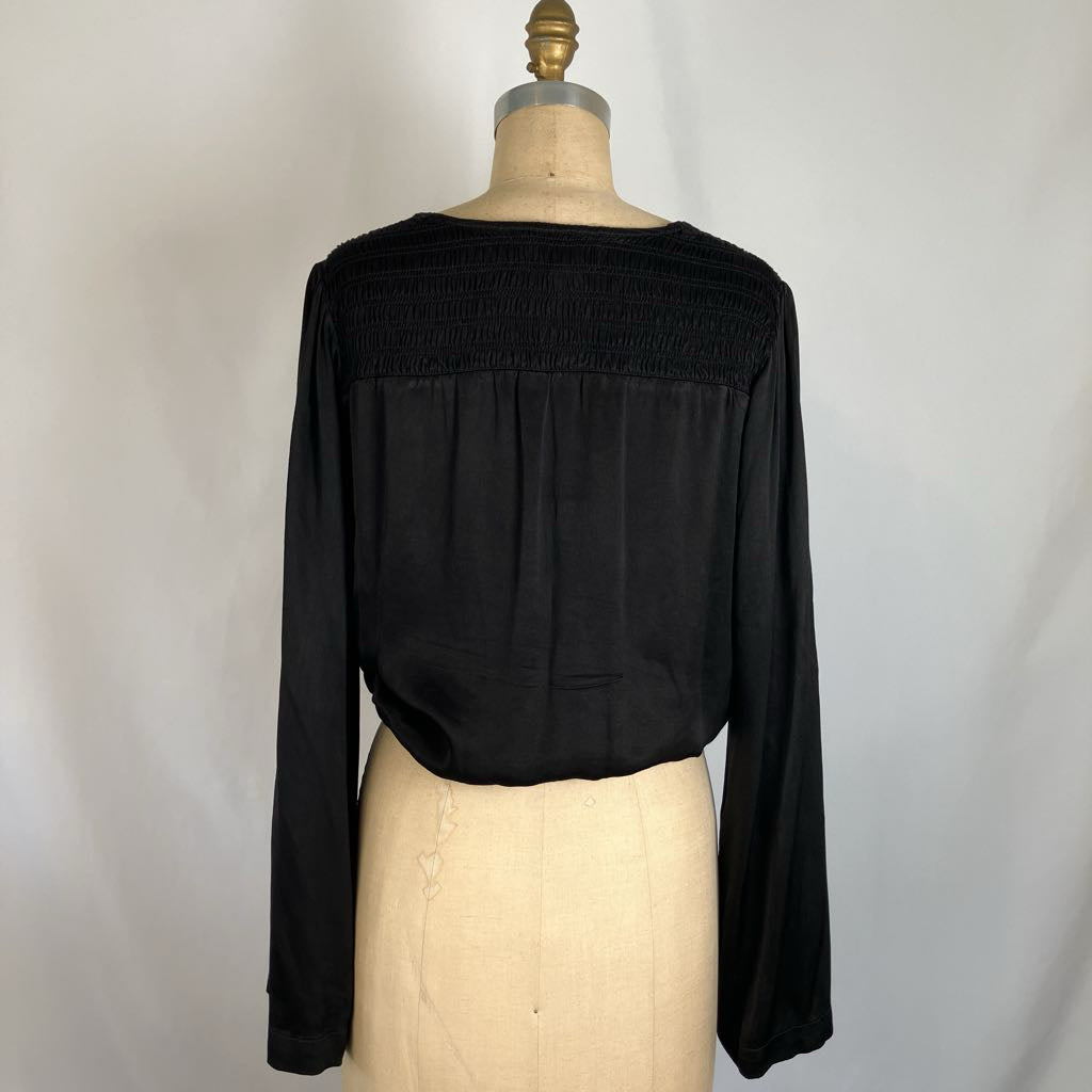 A black long-sleeve cropped top with a smocked yoke, displayed on a beige dress form mannequin against a light gray fabric backdrop.