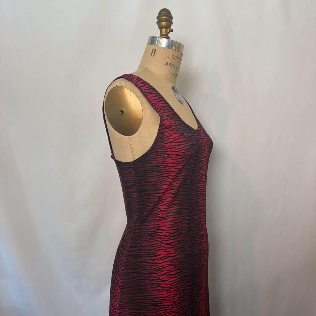 A sleeveless red and black patterned dress displayed on a wooden dress form mannequin against a light gray fabric backdrop.