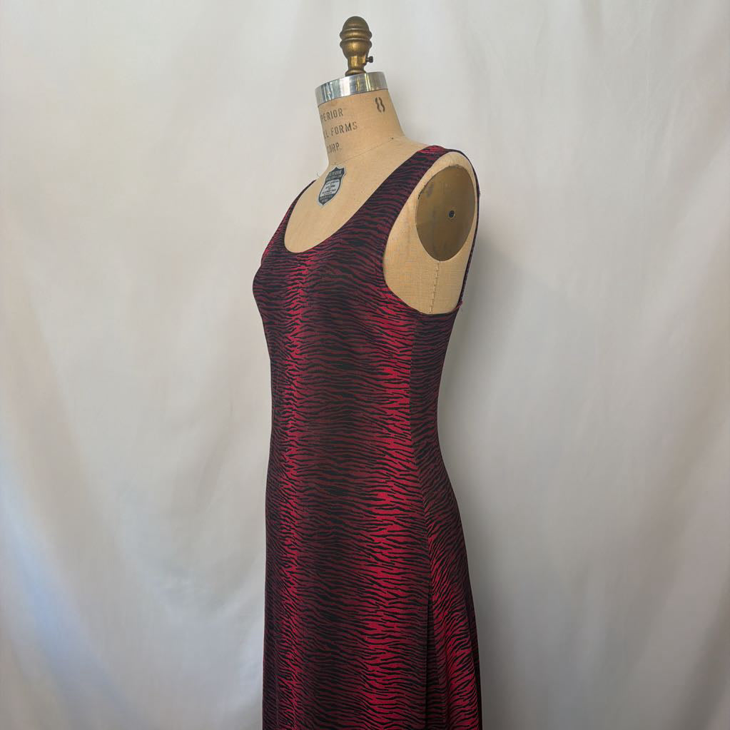 A sleeveless, scoop-neck maxi dress with a red and black wavy abstract pattern, displayed on a wooden dress form mannequin against a white fabric backdrop.