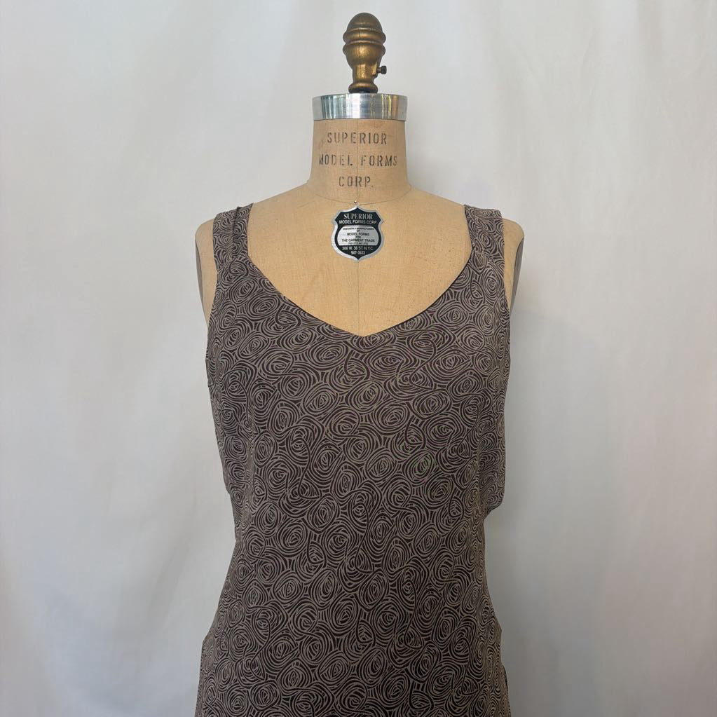 A sleeveless brown patterned dress displayed on a tan dress form mannequin against a light gray fabric backdrop.