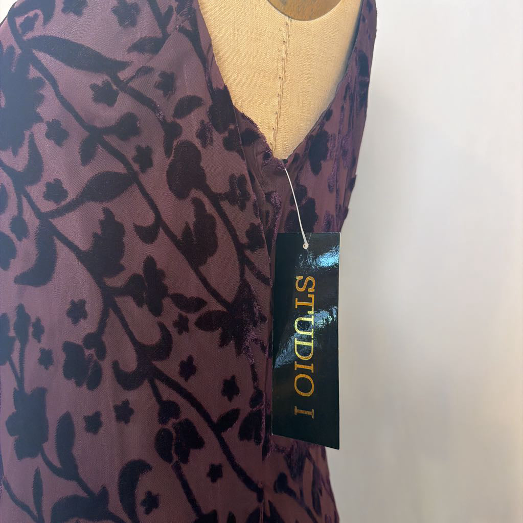 A close-up of a purple floral-patterned top displayed on a beige dress form, with a black hangtag reading STUDIO 1 attached.