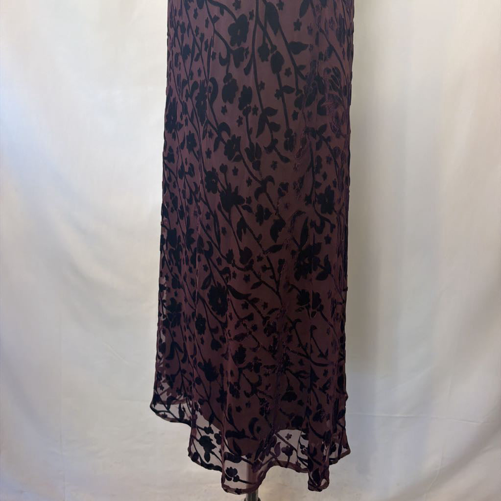 A sheer, dark purple midi-length skirt with a black floral vine pattern, displayed on a mannequin against a white fabric backdrop.