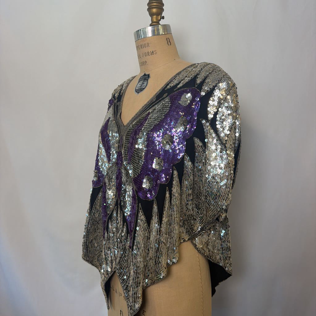 A vintage-style beaded cape top with silver and purple sequins, displayed on a tan dress form mannequin against a light gray fabric backdrop.