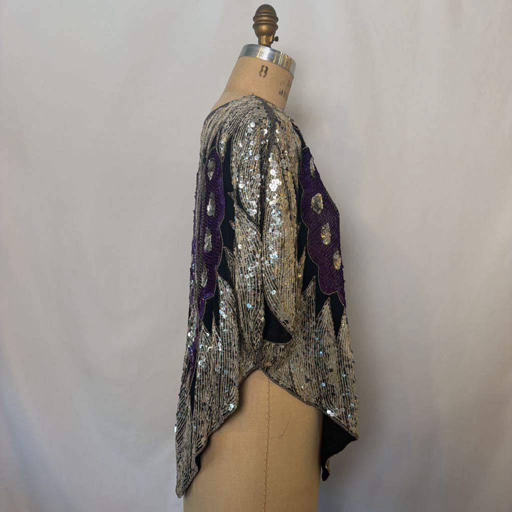 A sequined tunic top displayed on a dress form mannequin, featuring a silver and black sequin pattern with purple embroidered accents.