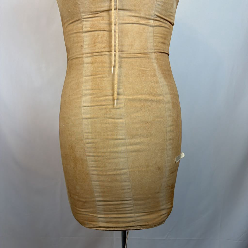 A tan/beige bodycon mini dress displayed on a dress form mannequin against a light gray fabric backdrop.