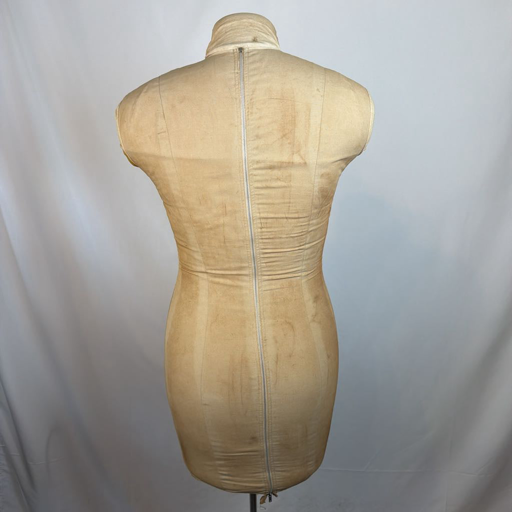 A beige fabric dress form mannequin shown from the back, featuring a full-length central zipper and a mock neck collar, set against a light gray fabric backdrop.