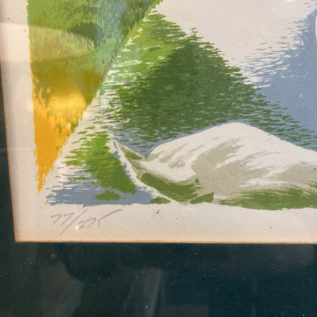 A close-up of a framed or mounted art print showing an abstract landscape-like composition with green, blue, white, and yellow brushstrokes, signed in the lower left corner.