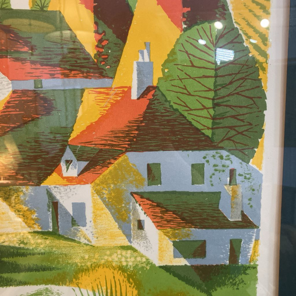 A close-up of a colorful art print or painting depicting stylized houses with red-orange roofs, green trees, and geometric shapes in yellow, green, orange, and white.