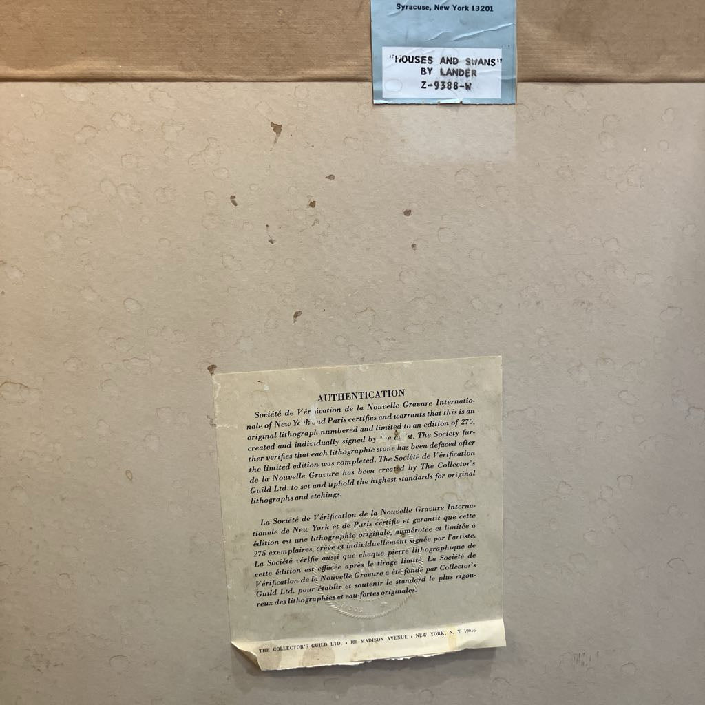 A beige cardboard surface with a small blue label at the top and a torn beige authentication paper note below.
