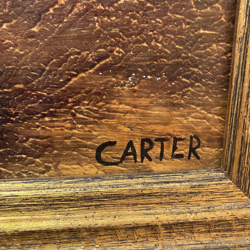 Close-up of a framed artwork corner showing a textured warm brown surface with the name CARTER in black script and a rustic wooden frame.