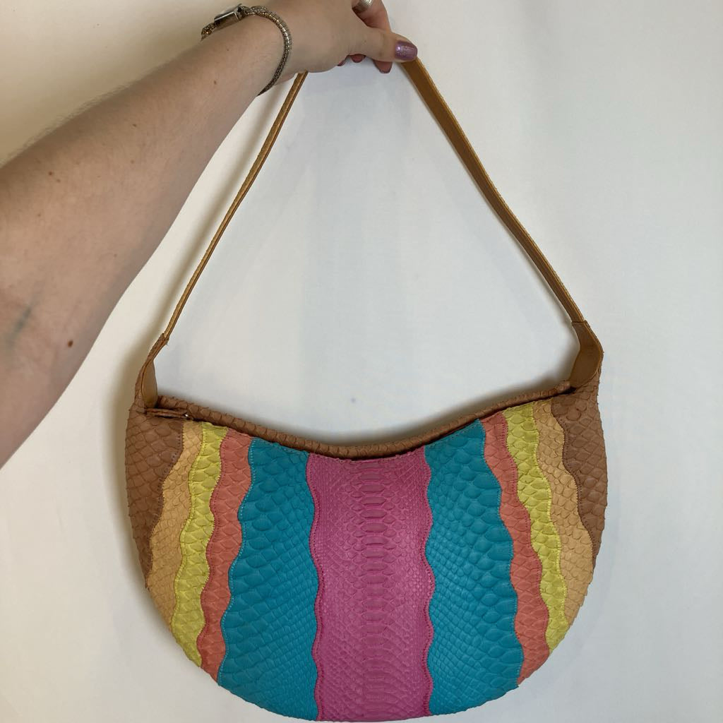 A handbag with a curved brown leather strap, held by a person's arm. The bag features a colorful, wavy vertical stripe pattern in turquoise, magenta, orange, yellow, and brown textured faux-leather panels, set against a plain off-white background.