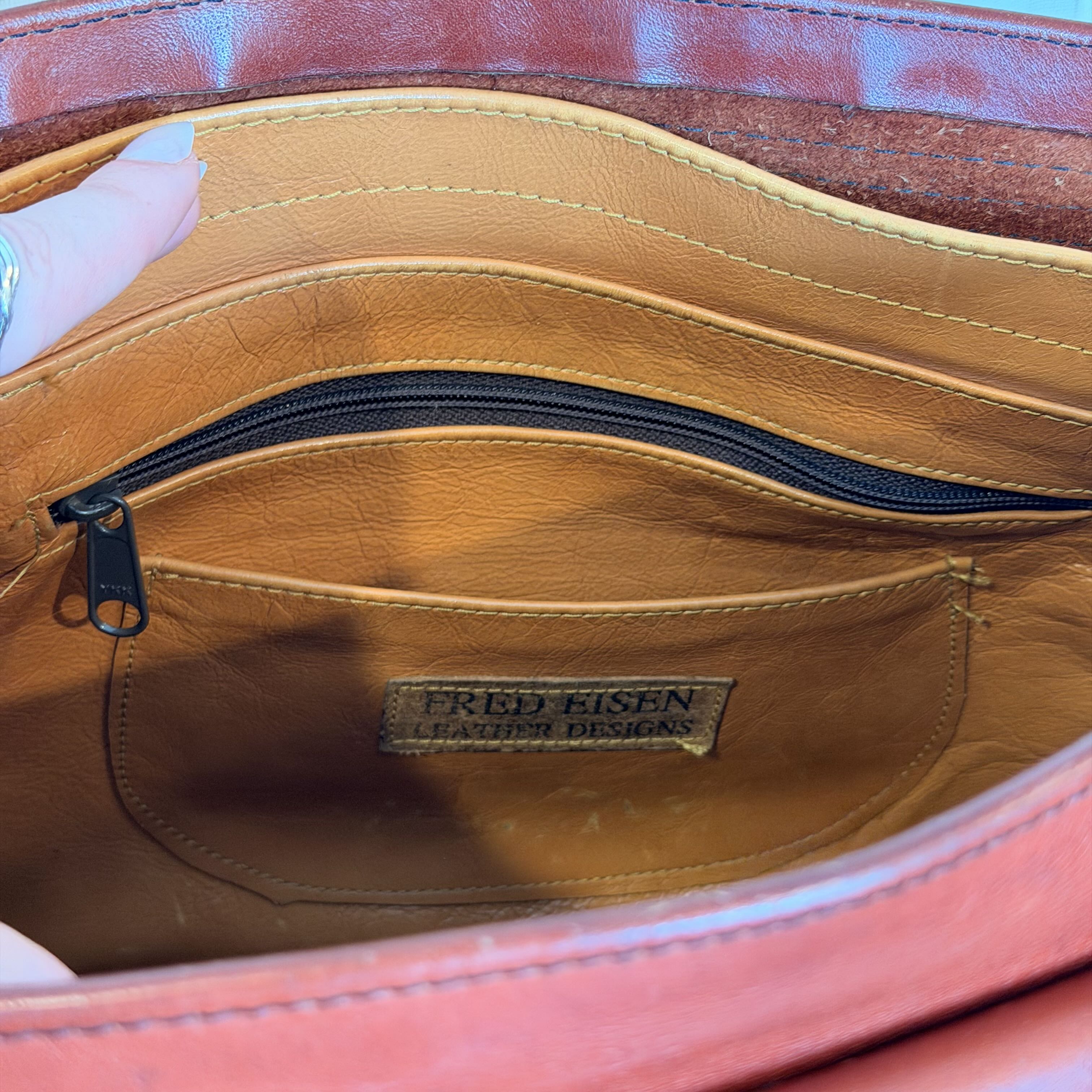 Close-up of the interior of a Fred Eisen leather bag, showing a tan leather pocket with a black zipper and a visible Fred Eisen Leather Designs brand label.
