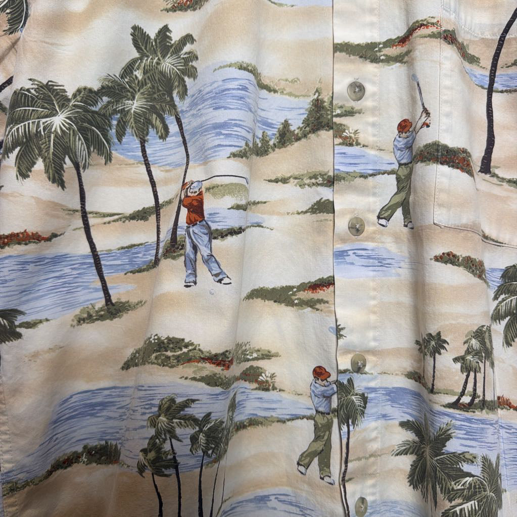 Close-up of a button-front garment with an allover golf course print featuring palm trees, sand, blue water, and golfers. The fabric fills the frame.