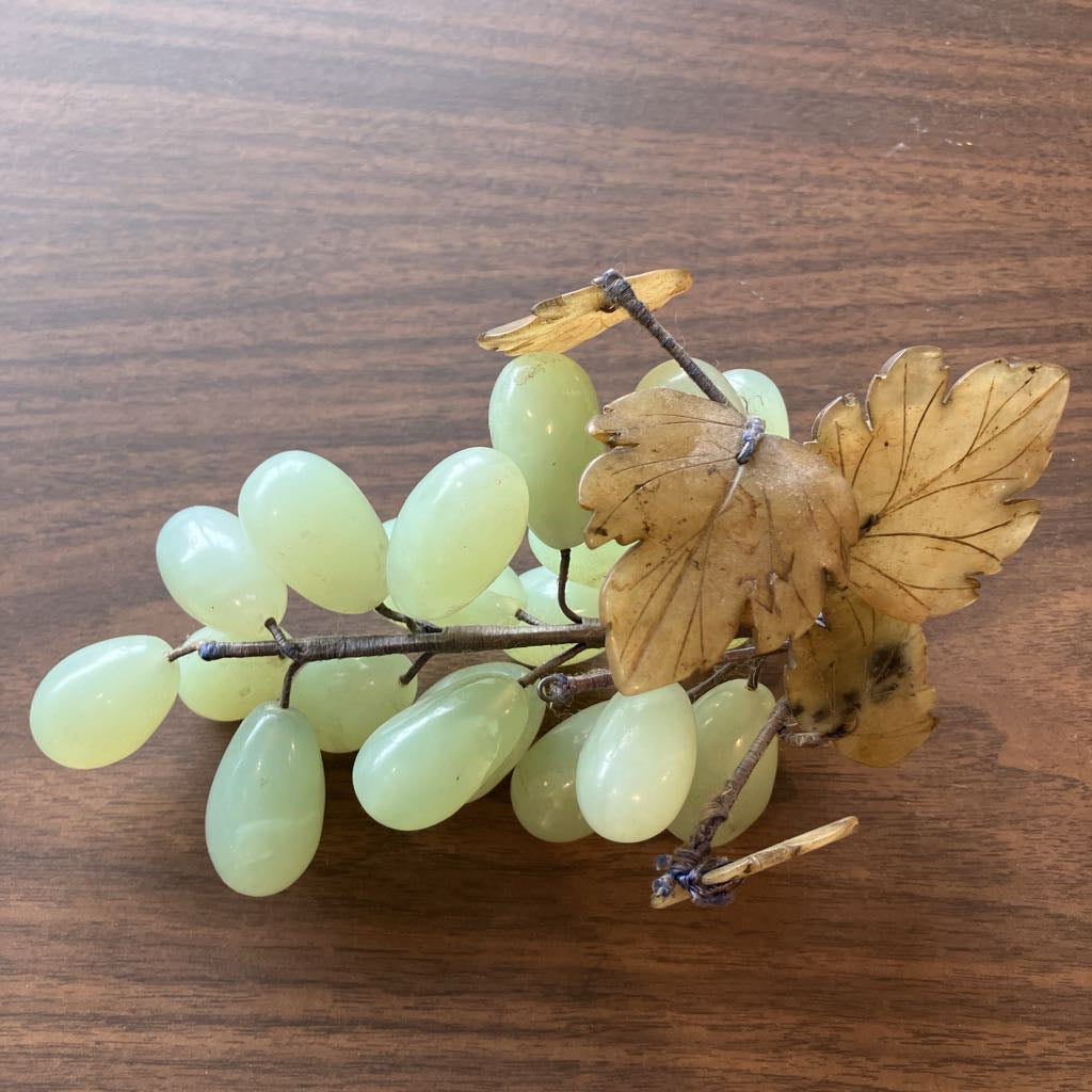 A decorative grape cluster sculpture with pale green translucent grapes and brown leaf accents, displayed on a wooden surface.
