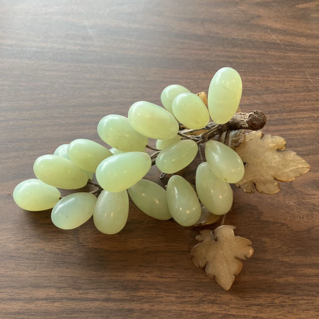 A decorative grape cluster prop with pale green oval grapes and tan leaves, placed on a brown wooden surface.