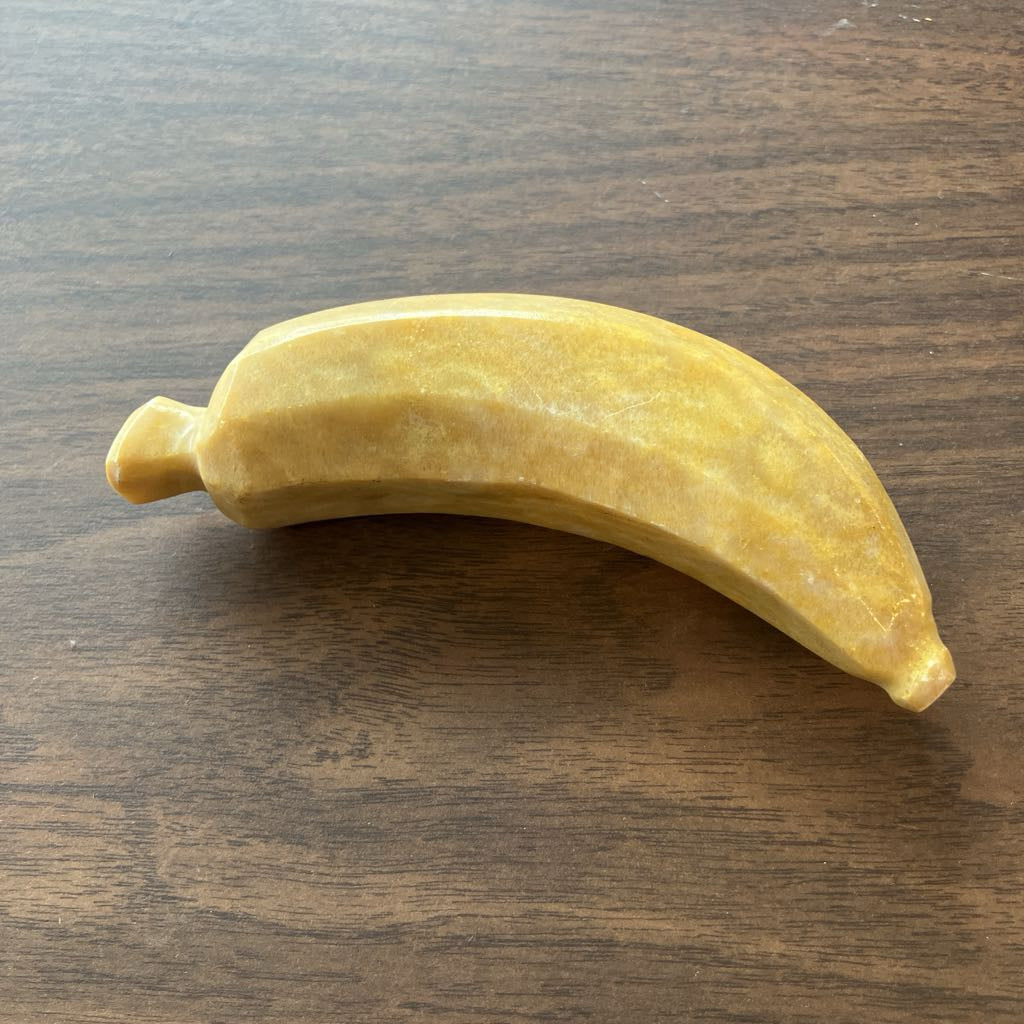A carved yellow stone banana figurine resting on a dark brown wooden surface.