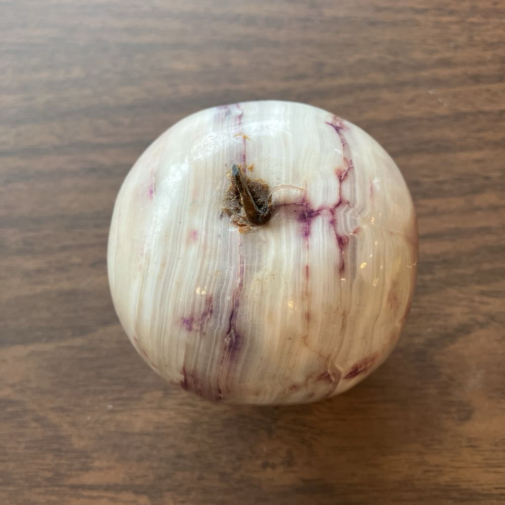 A polished round stone object with a creamy off-white base and natural purple marbling, photographed from above on a brown wooden surface.