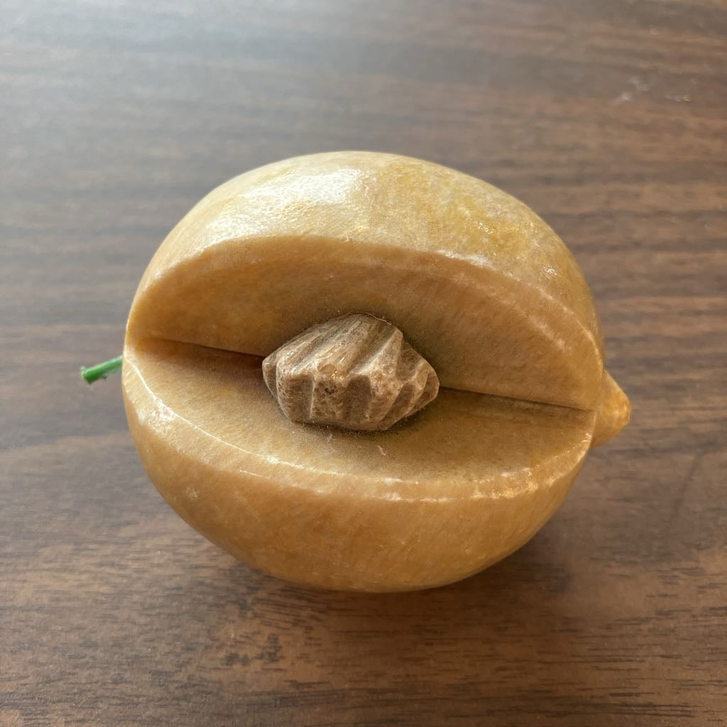 A carved stone fruit sculpture or decorative object shaped like a split peach or apricot with a small green stem, displayed on a dark wood surface.
