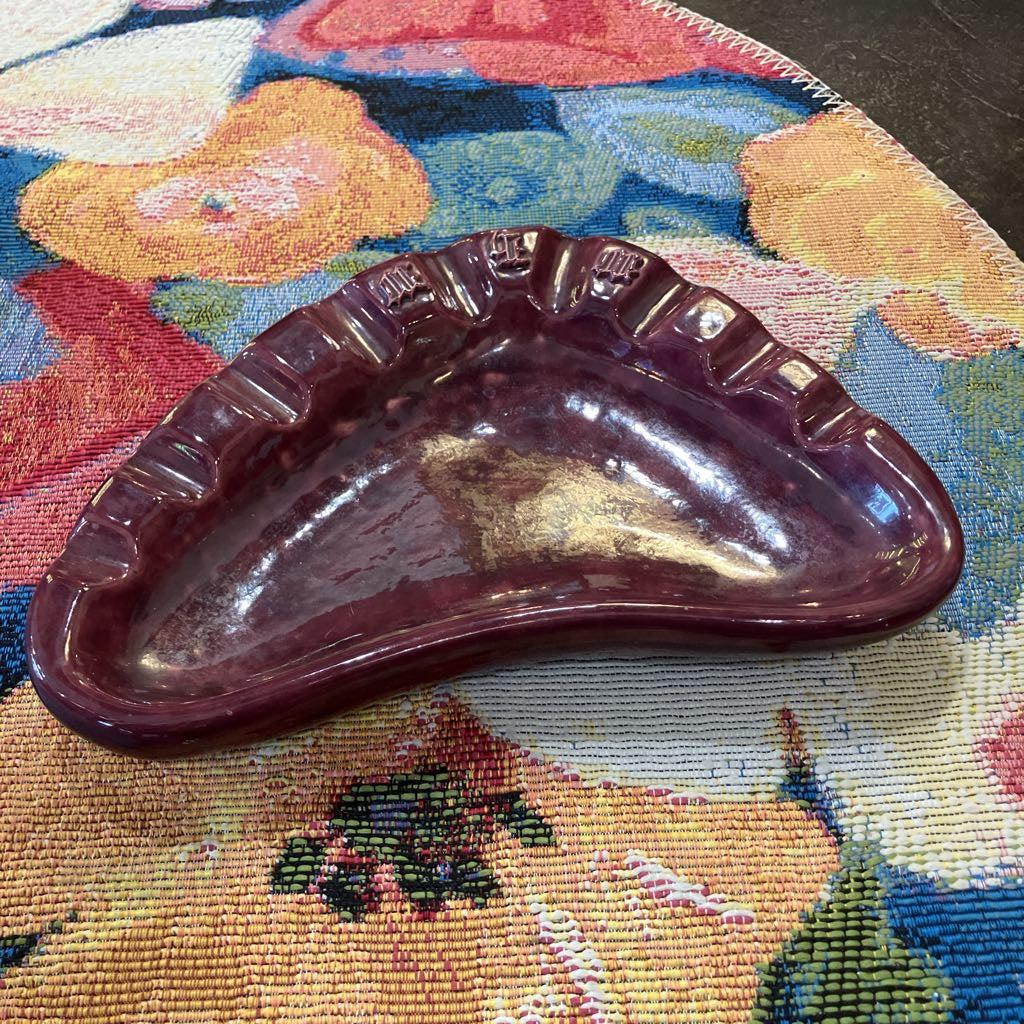 A glossy, dark burgundy ceramic dish with a scalloped rim, resting on a colorful floral tapestry rug.