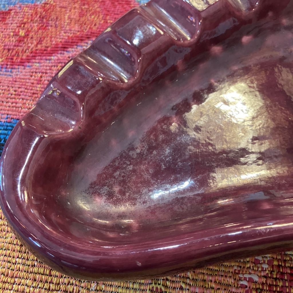 A close-up of a glossy, maroon-brown glass dish with a scalloped rim, resting on a textured woven mat.
