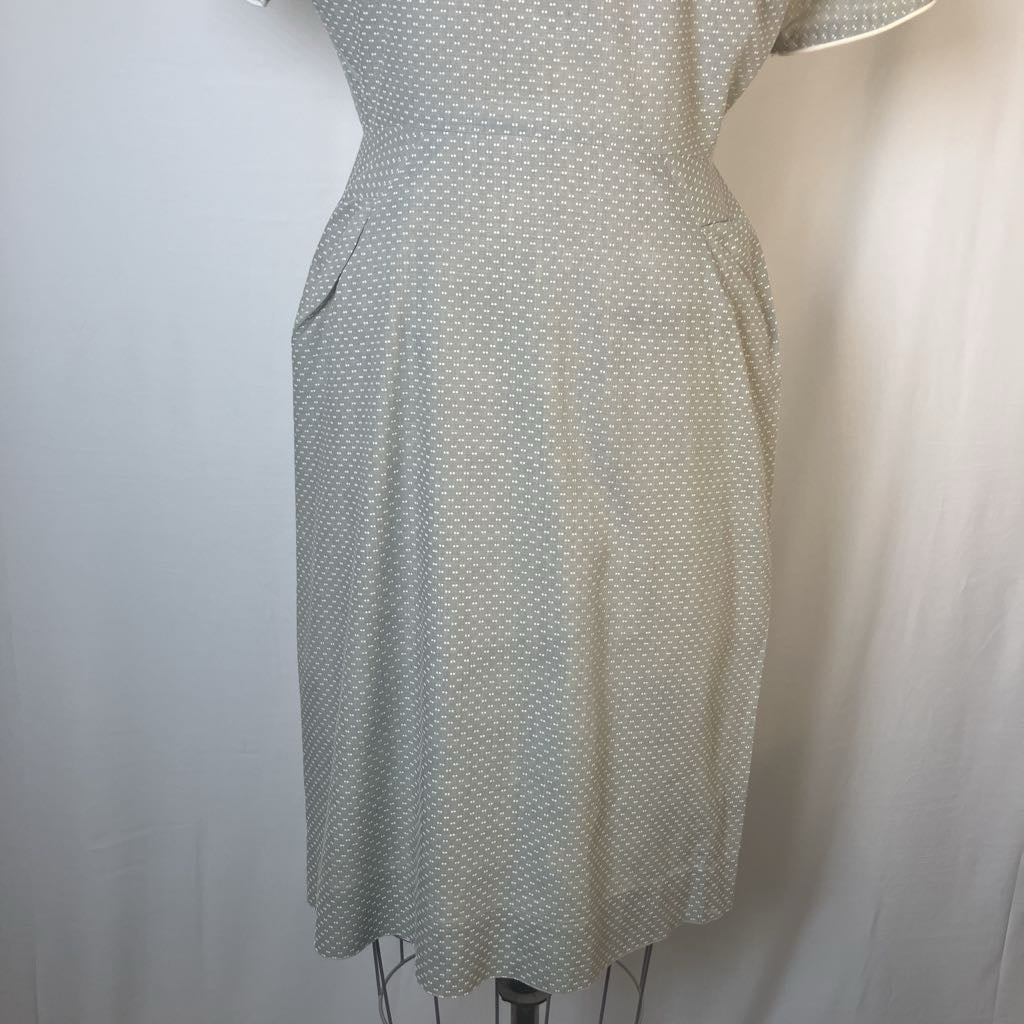 A short-sleeve knee-length dress with a small white polka dot pattern on a light beige or cream base, displayed on a dress form against a white fabric backdrop.