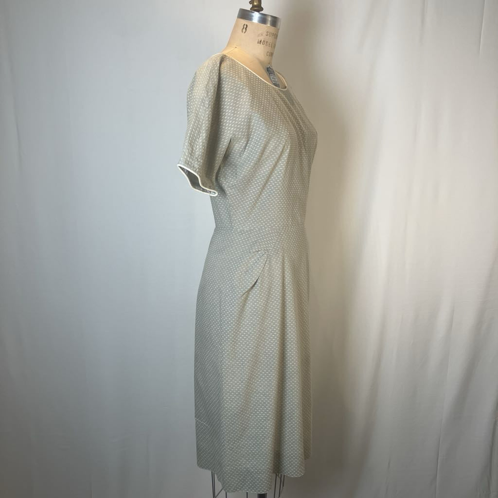 A short-sleeve knee-length dress with a small repeating geometric pattern, displayed on a vintage dress form mannequin against a white fabric backdrop.