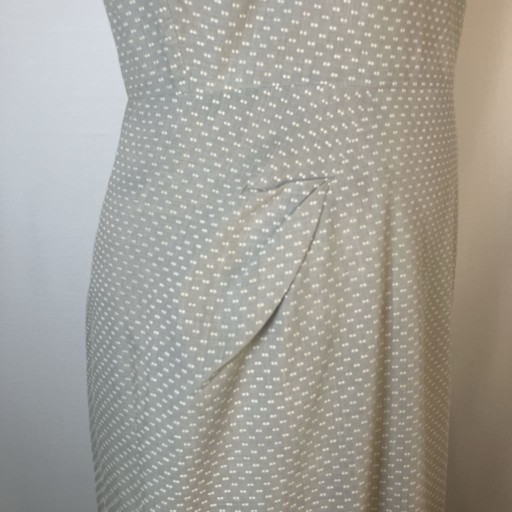 A close-up of a light beige or cream dress with a small white geometric dot pattern, featuring a side tie detail at the waist.