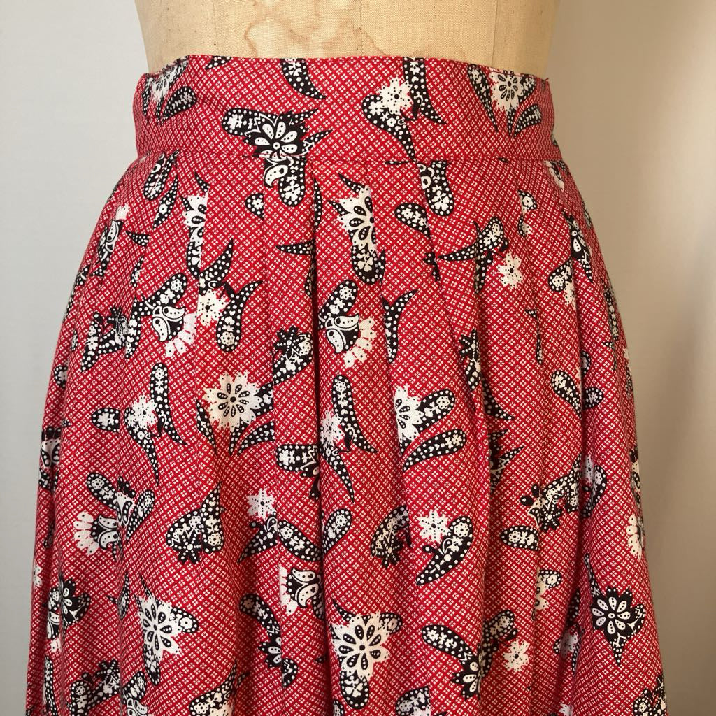 A red high-waisted skirt with a black and white butterfly and floral pattern, displayed on a beige dress form against a light beige background.