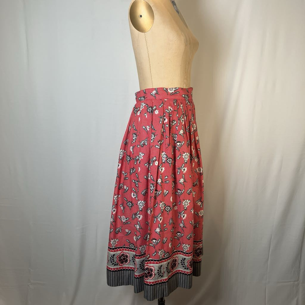 A pink floral midi skirt with a striped and patterned hem, displayed on a beige mannequin torso against a white fabric backdrop.