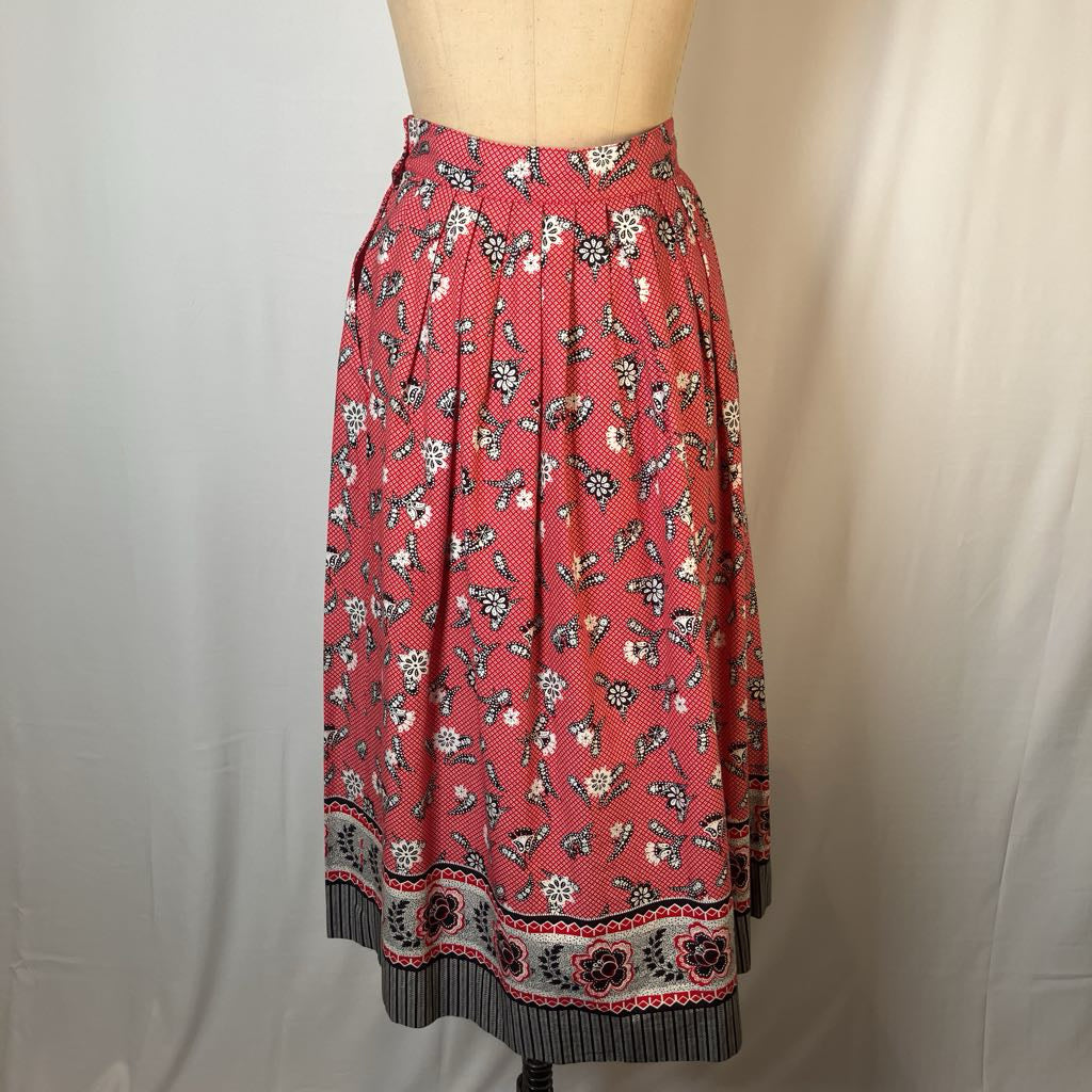 A red midi skirt with a black and white floral print and a decorative border, displayed on a beige dress form against a white fabric backdrop.