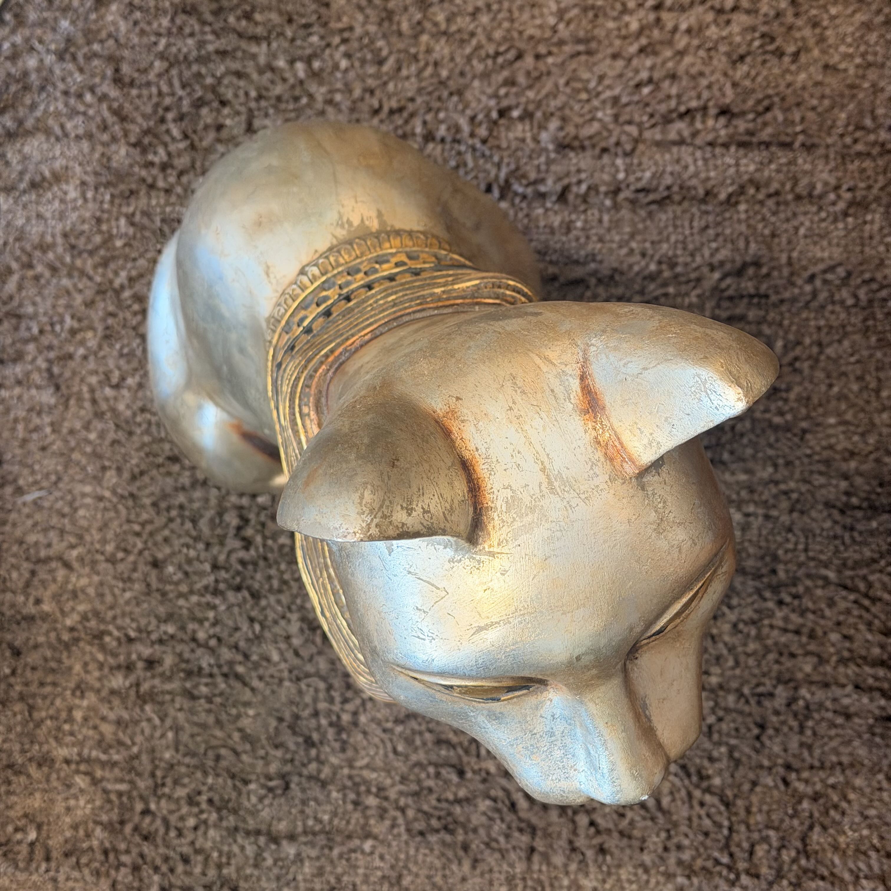 A small sculpted cat figurine in a metallic gold finish, lying on a brown textured carpet.