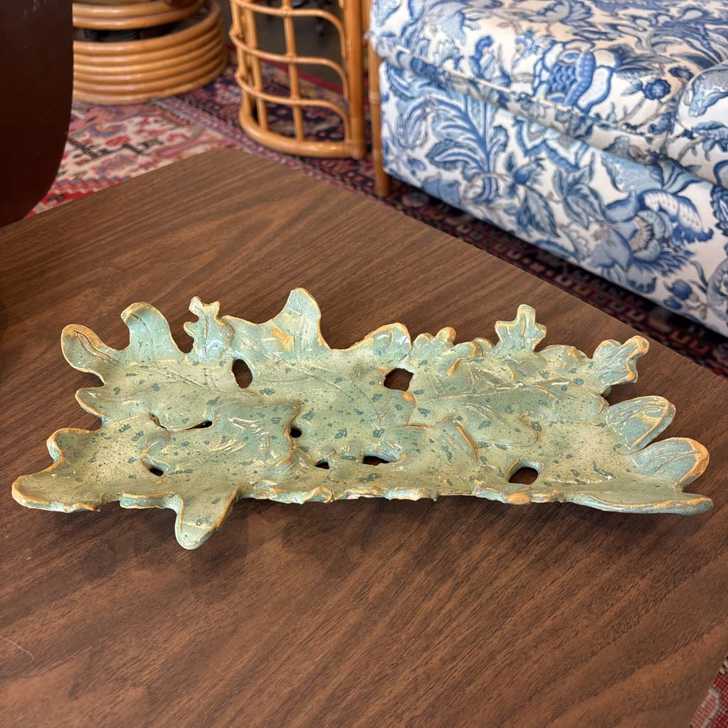 A green ceramic tray of leaves pieced together on a wooden surface and in a store setting.