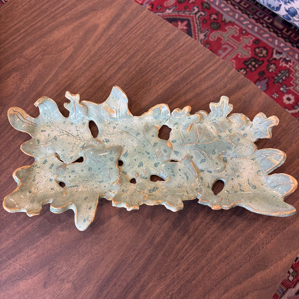 A green ceramic tray of leaves pieced together on a wooden surface and in a store setting.