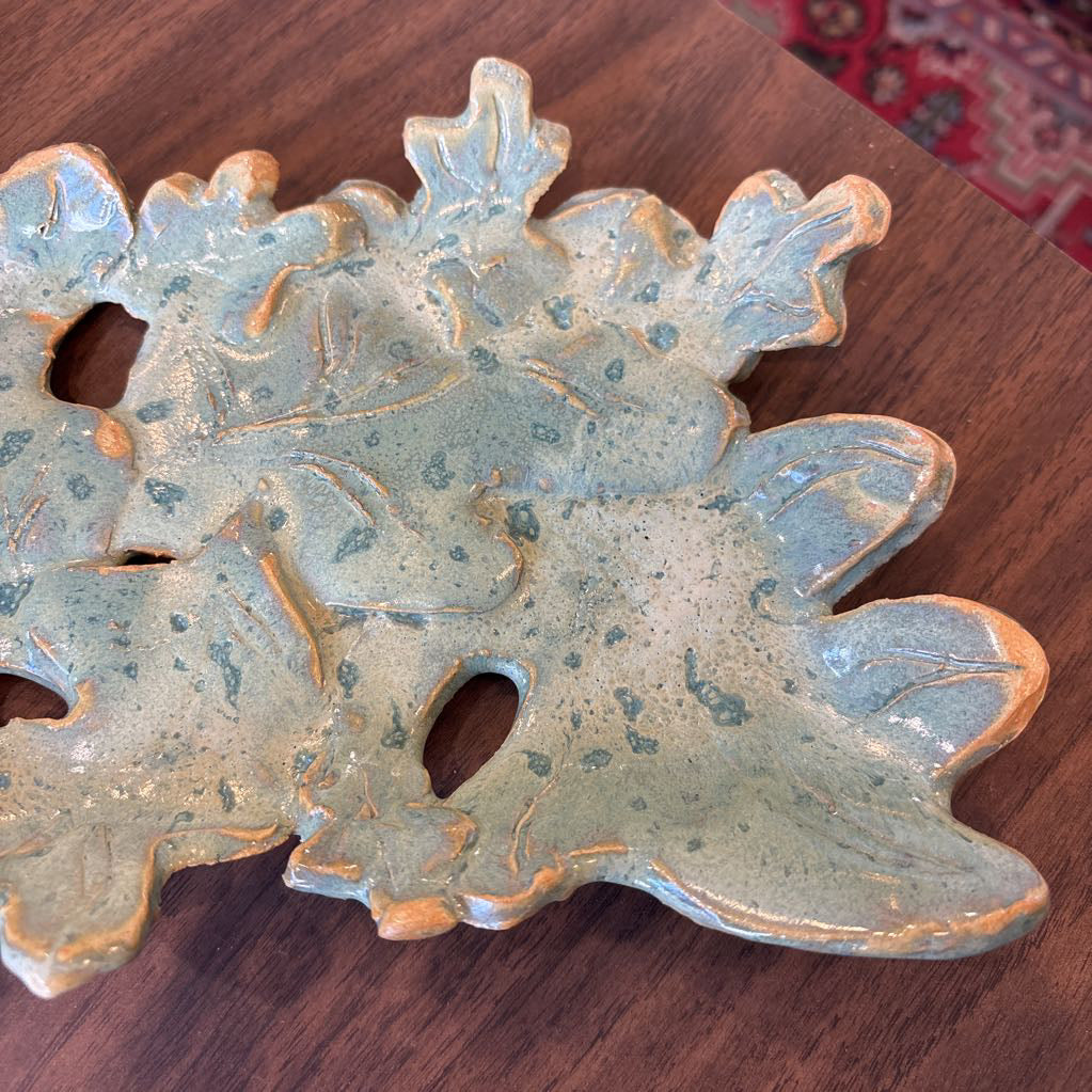 A green ceramic tray of leaves pieced together on a wooden surface and in a store setting.