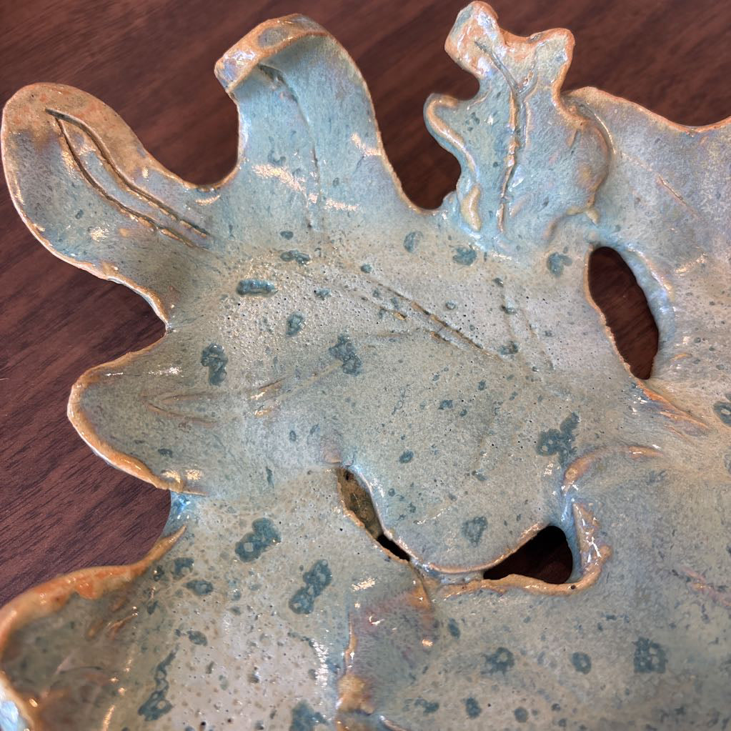 A green ceramic tray of leaves pieced together on a wooden surface and in a store setting.