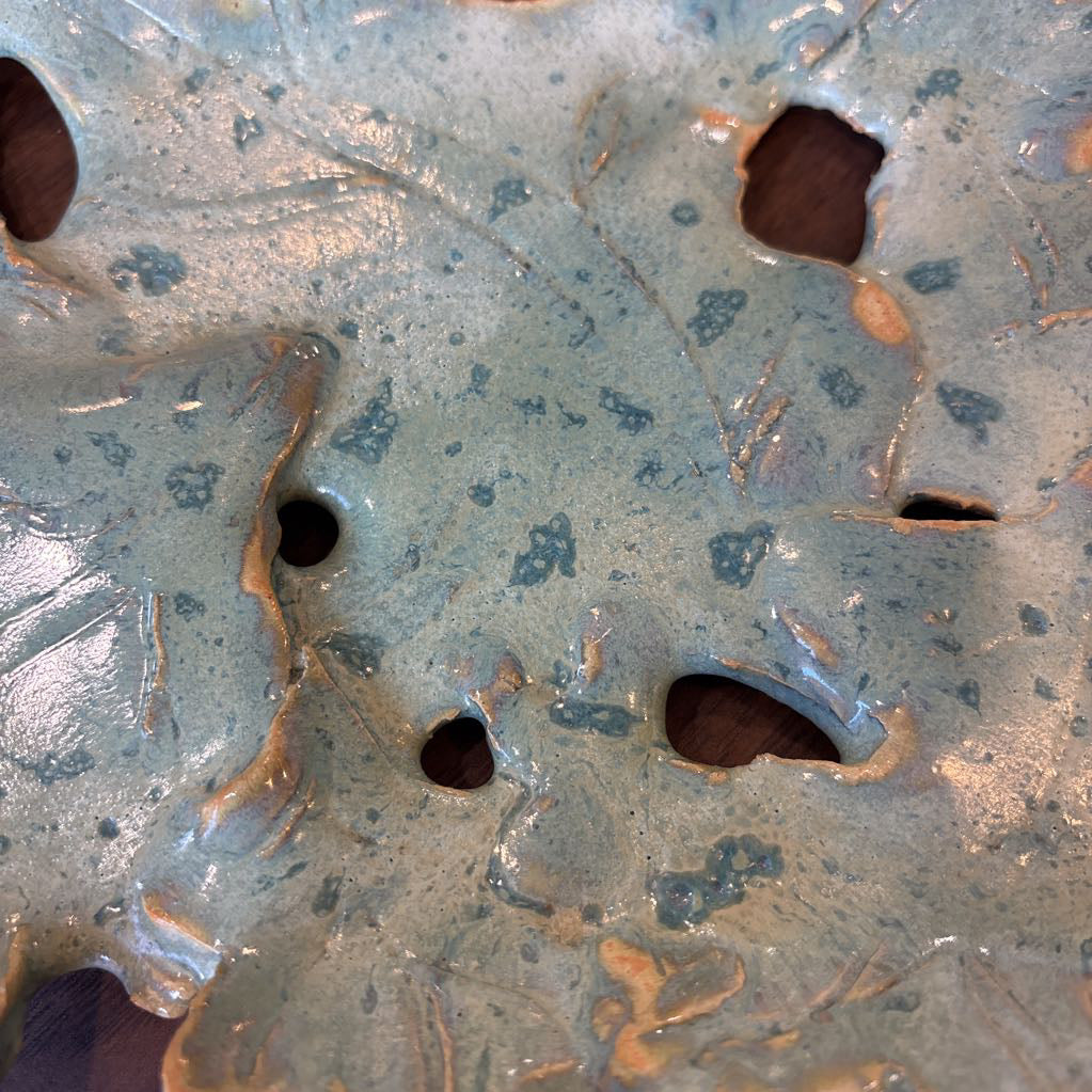 A green ceramic tray of leaves pieced together on a wooden surface and in a store setting.