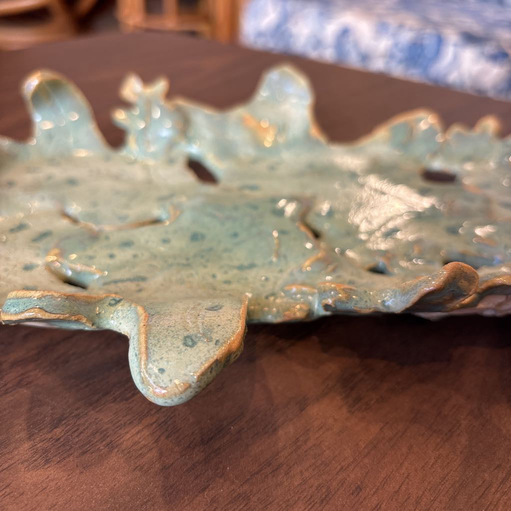 A green ceramic tray of leaves pieced together on a wooden surface and in a store setting.
