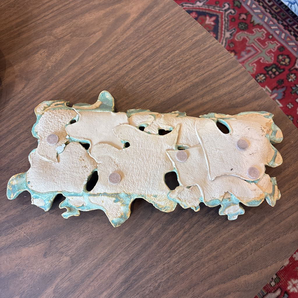 A green ceramic tray of leaves pieced together on a wooden surface and in a store setting.