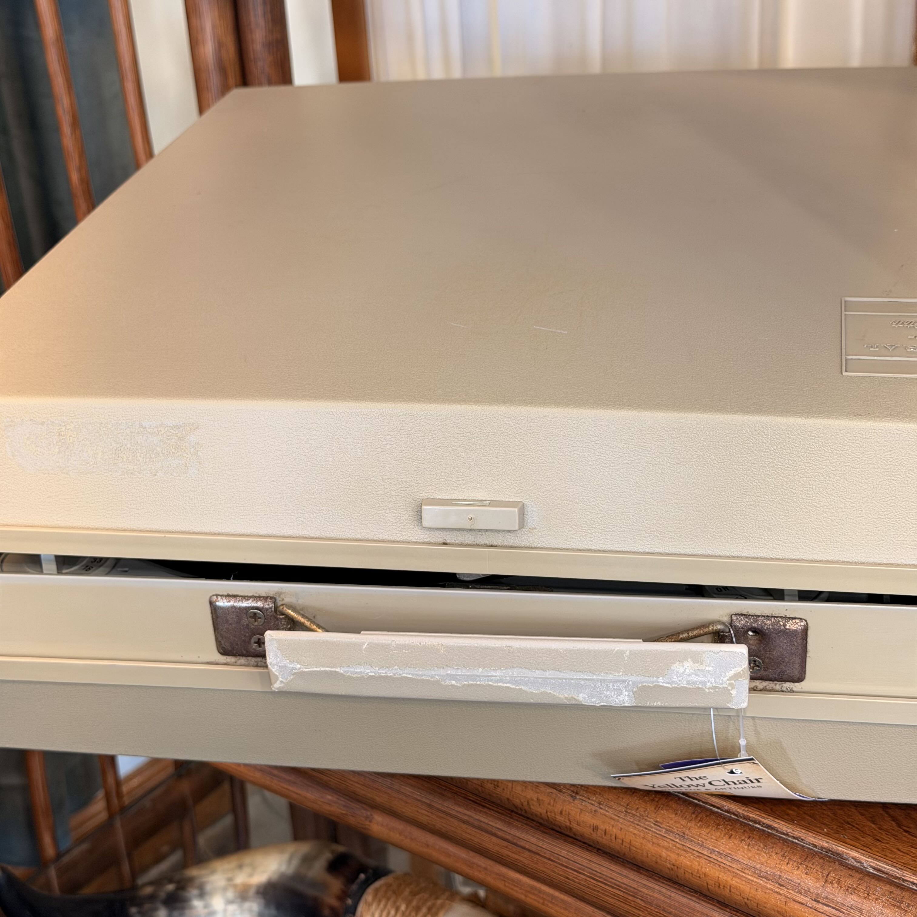 A vintage beige plastic drawer or storage unit with a pull handle wrapped in white tape, sitting on a wooden surface.