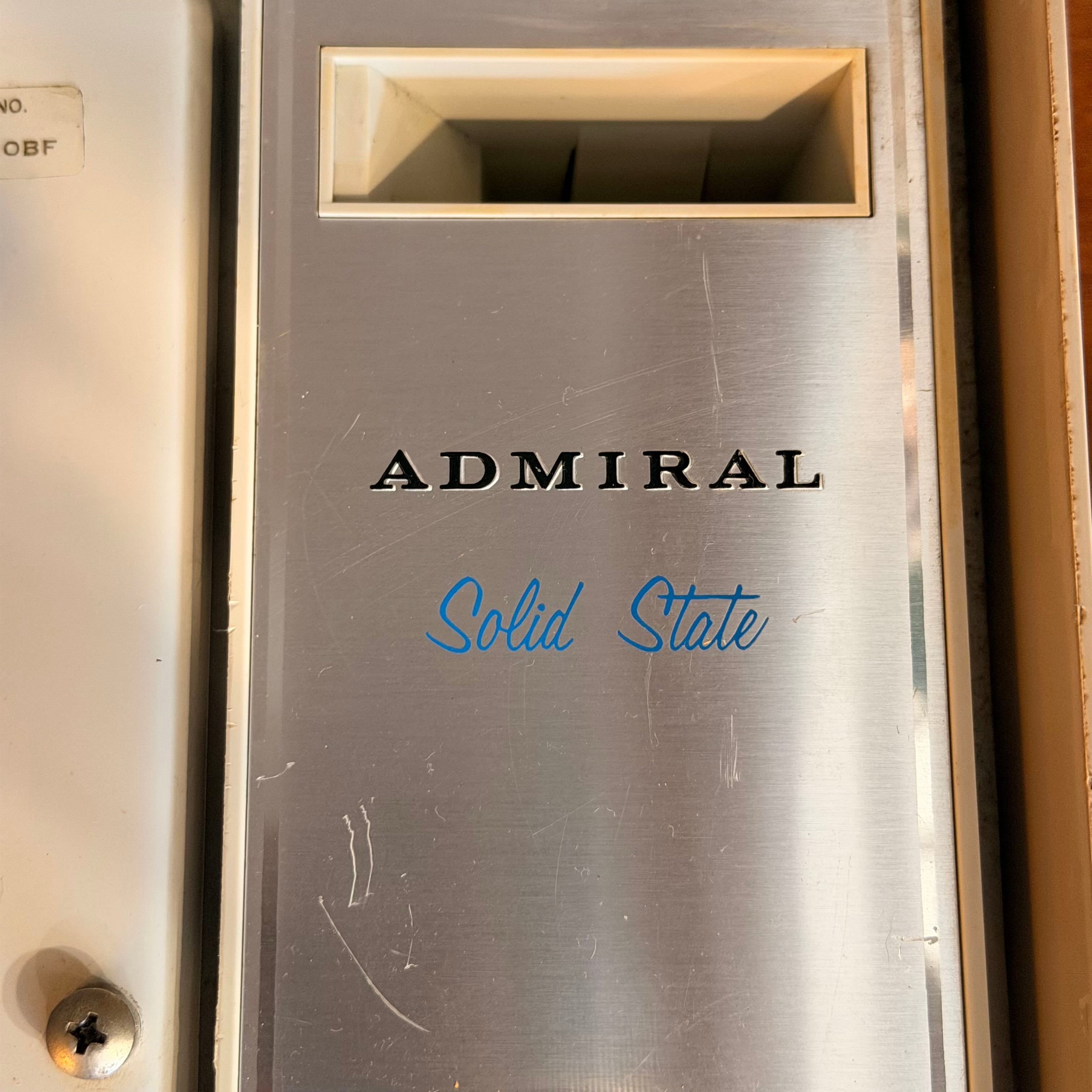 A brushed stainless steel door stopper or wall-mounted fixture with the word ADMIRAL in black lettering and blue script reading 'Solid State' underneath, shown in a close-up indoor shot.
