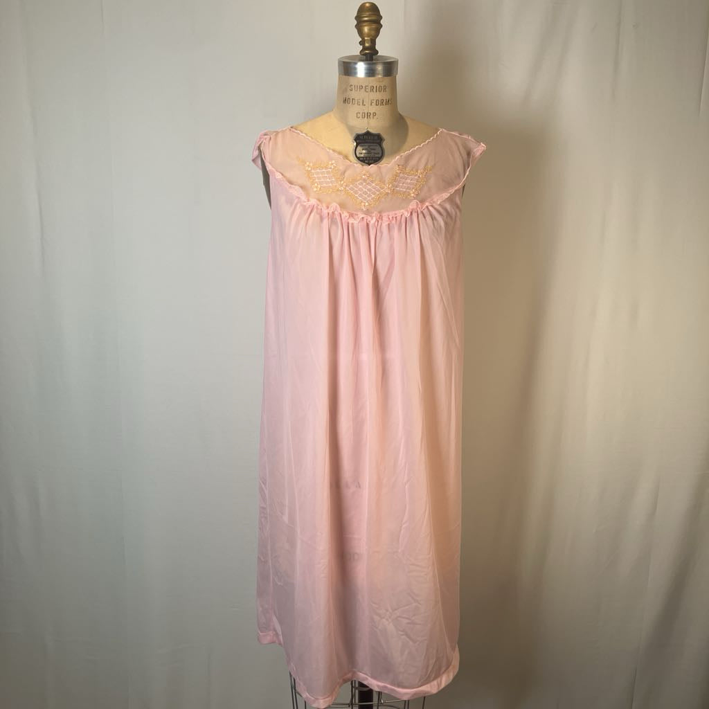 A light pink nightgown displayed on a vintage dress form mannequin against a neutral off-white fabric backdrop.