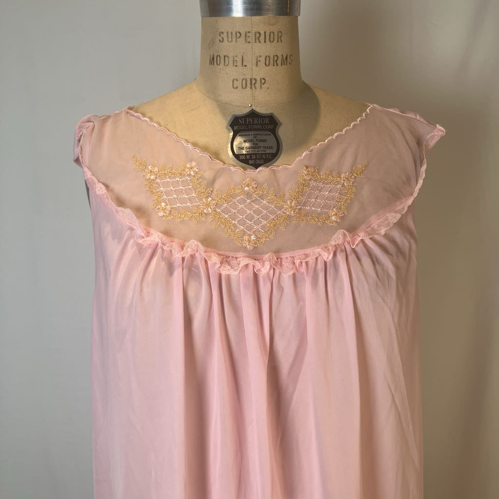 A light pink nightgown with a scalloped ruffled neckline and gold embroidered geometric patterns, displayed on a vintage mannequin torso.