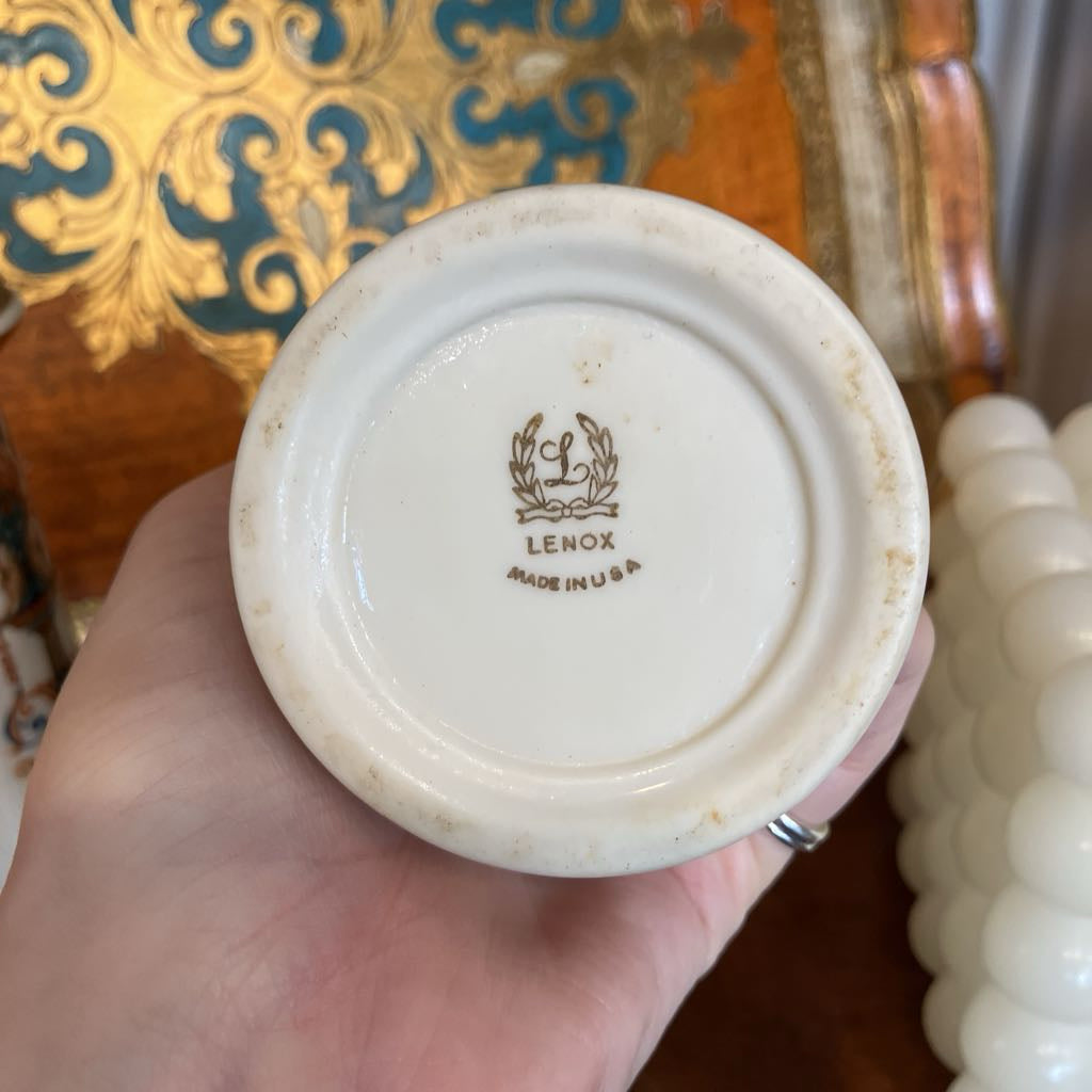 A hand holding the bottom of a vintage Lenox ceramic container, showing the white porcelain base with the brown 'Lenox Made in USA' logo.