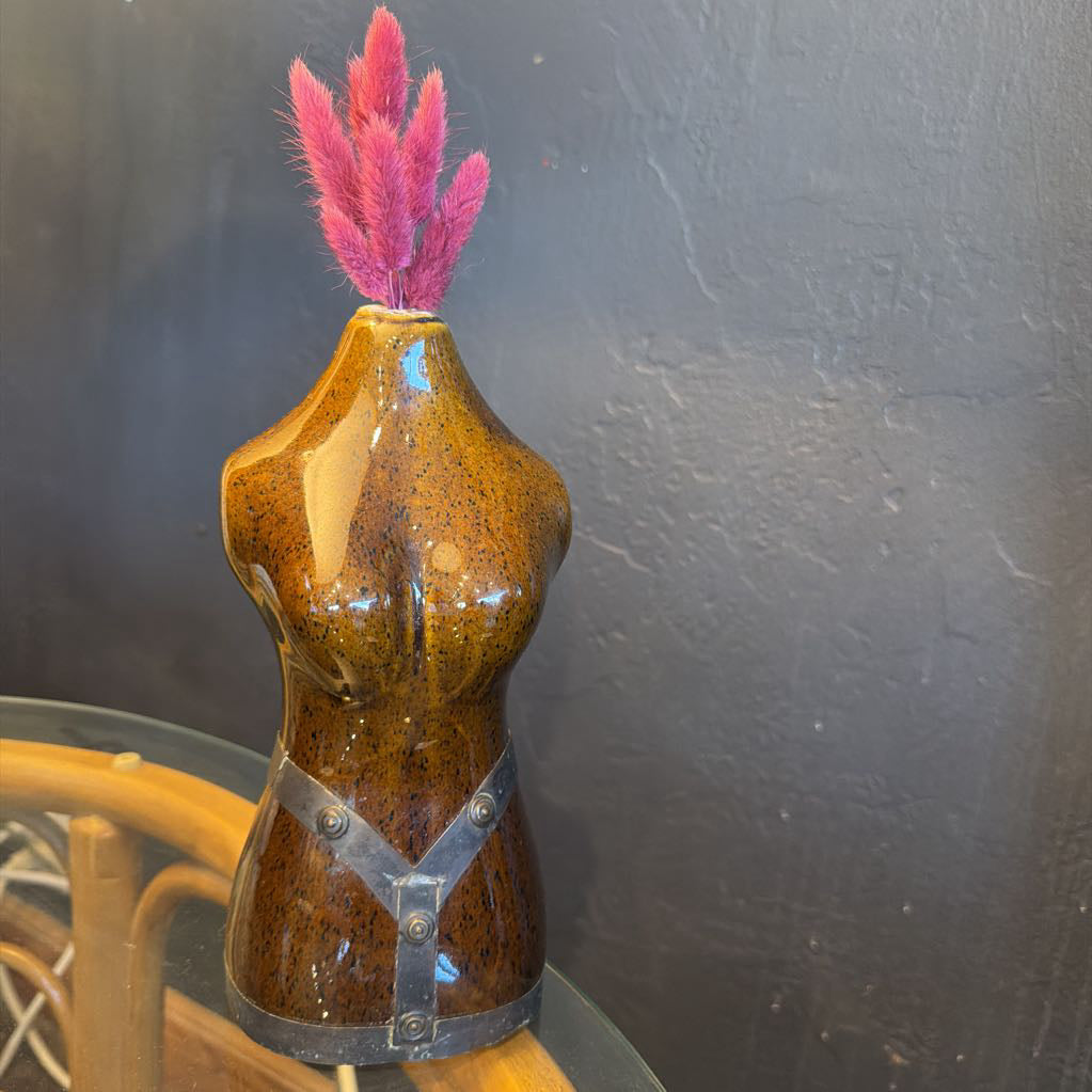 Brown ceramic female torso with metal vase with a few pink flowers coming out