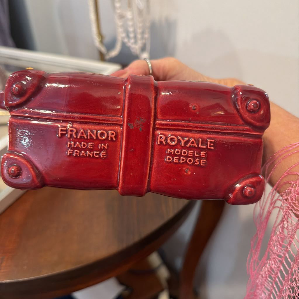 A hand holding a glossy red ceramic French trunk figurine with embossed text reading 'FRANOR MADE IN FRANCE' and 'ROYALE MODELE DEPOSE'.