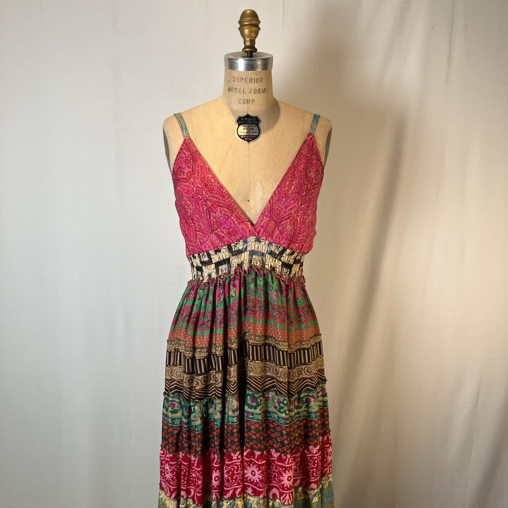 A sleeveless bohemian-style maxi dress with a vibrant pink patterned bodice and a multicolor patterned skirt, displayed on a vintage mannequin against a neutral fabric backdrop.