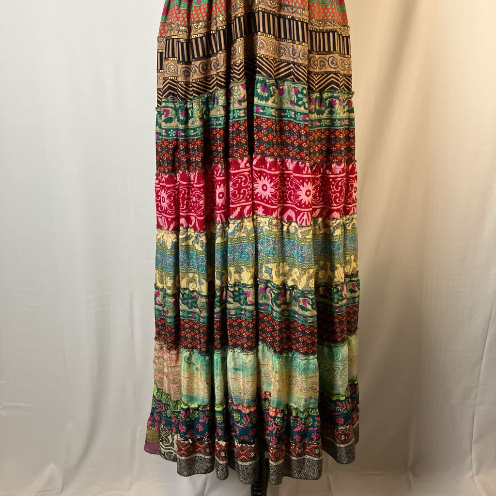 A long bohemian maxi skirt with a colorful horizontal striped pattern featuring red, green, blue, yellow, and brown motifs, displayed on a black dress form against a white fabric backdrop.